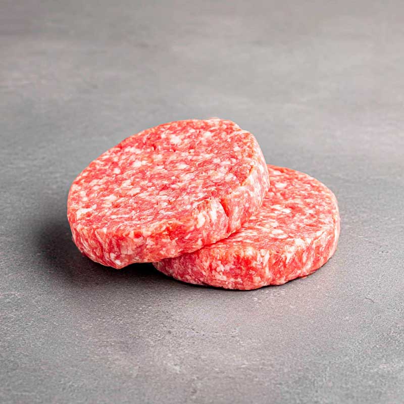 Zwei rohe Rinder-Patties (Burger-Patties) mit sichtbarer Fettmarmorierung auf grauem Steinuntergrund.