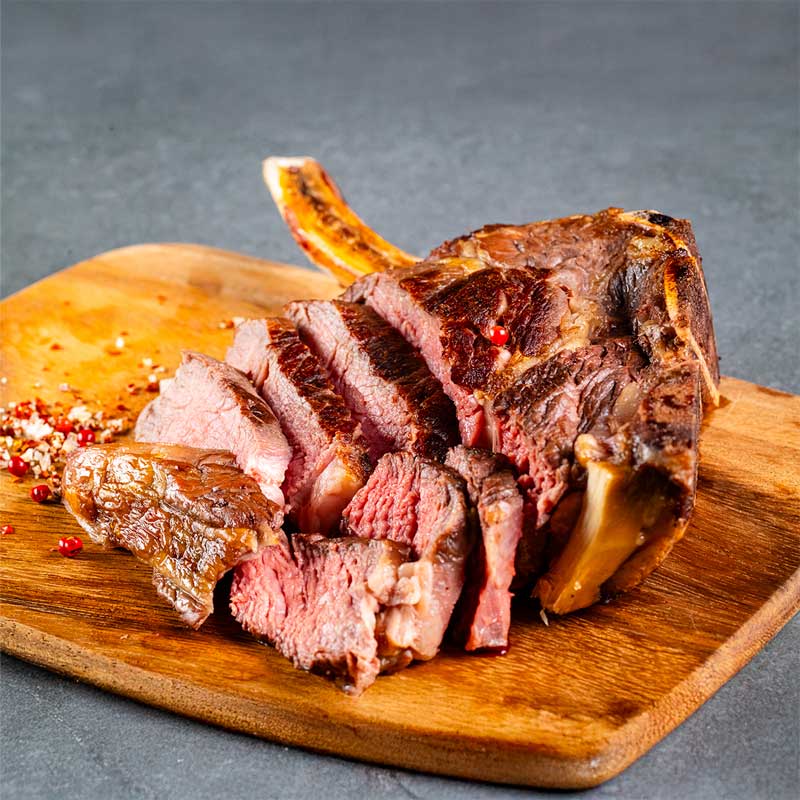 Gegrilltes Cowboysteak am Knochen von TAURBULL, Black Angus Steak, zart und mit aromatischer Kruste, aufgeschnitten auf Holzbrett