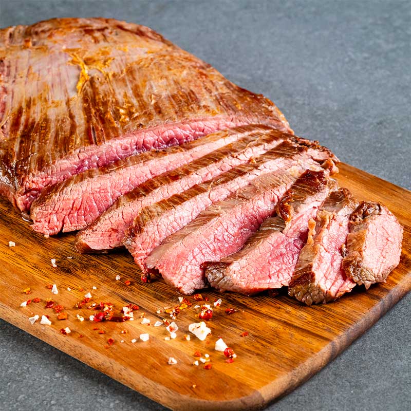 Gegrilltes Flank Steak von TAURBULL, Black Angus, aromatisch und saftig, aufgeschnitten in Scheiben auf Holzbrett