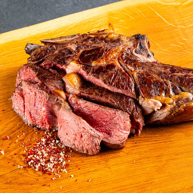 Beeindruckendes Tomahawk Steak von TAURBULL, Premium Black Angus Steak, knusprige Kruste und saftiger Kern, in Scheibe geschnitten, gegrillt