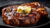Gegrilltes Ribeye-Steak mit geschmolzener Kräuterbutter auf einer heißen Pfanne.